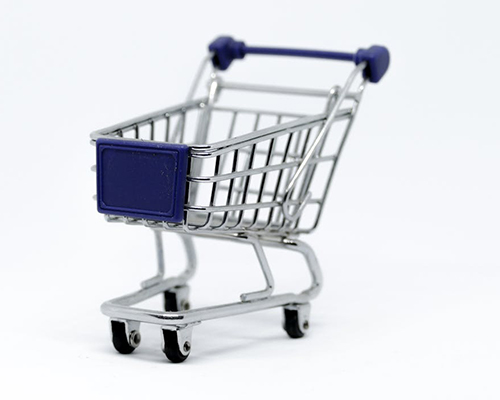 A close shot of a blue and silver toy shopping cart which looks slightly real, with a plain off-white background